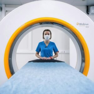 Nurse in blue scrubs and mask stands by an MRI machine, ready for a scan.