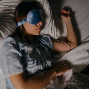 Woman peacefully sleeping with a blue eye mask in a cozy bed setting, promoting restful sleep.